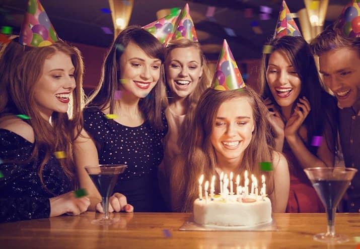 Freundinnen mit Partyhüten vor einer Geburtstagstorte mit Kerzen